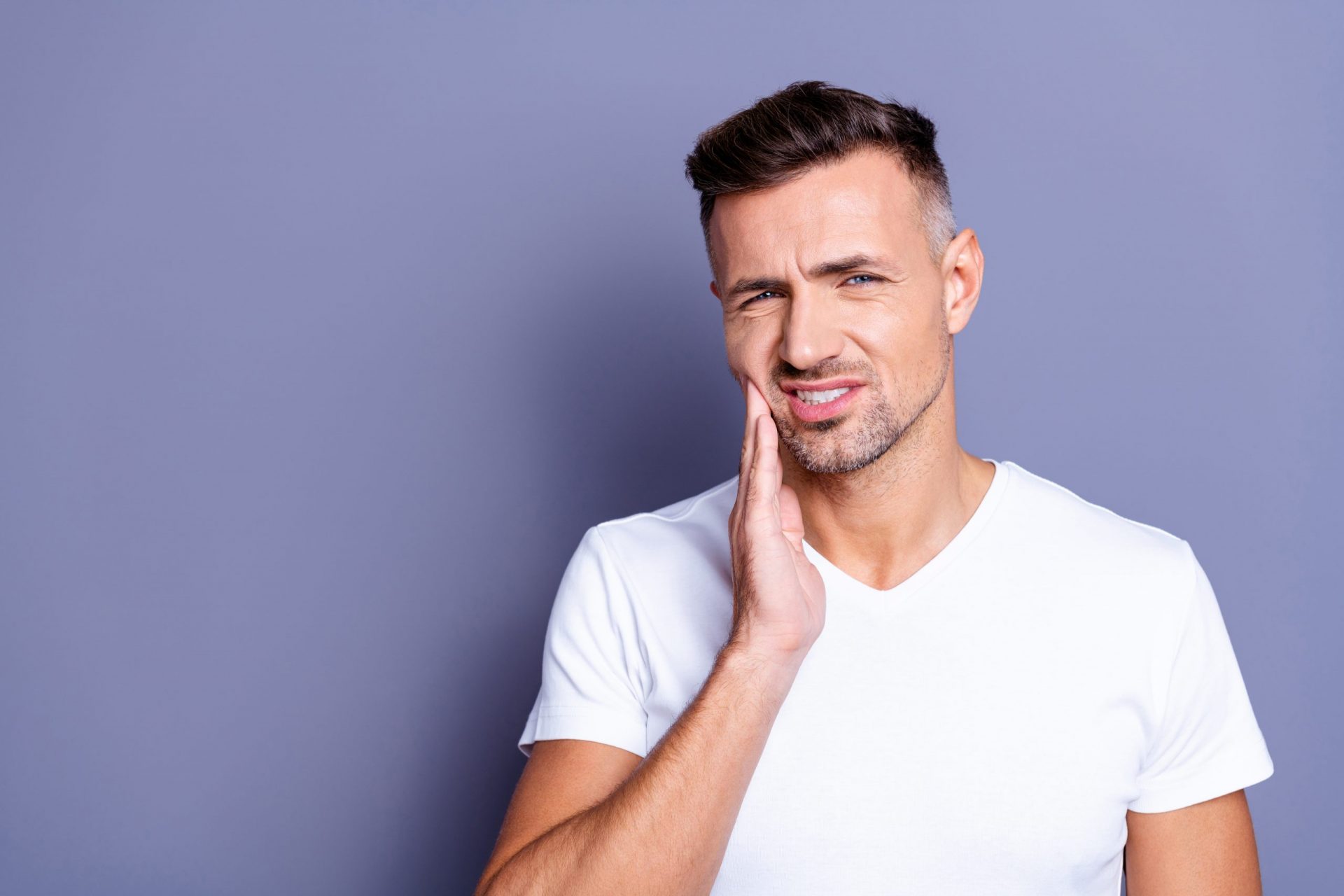 Man has jaw pain caused by malocclusion and is holding his cheek.