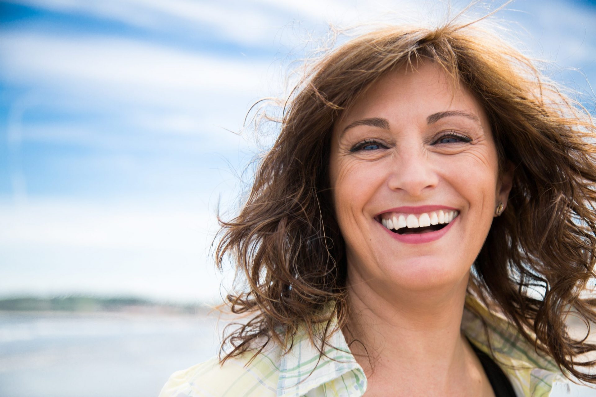 Woman with dental implants smiles with blue sky backdrop.