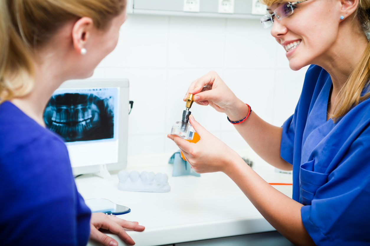 Lady dentist showing dental implant to the patient