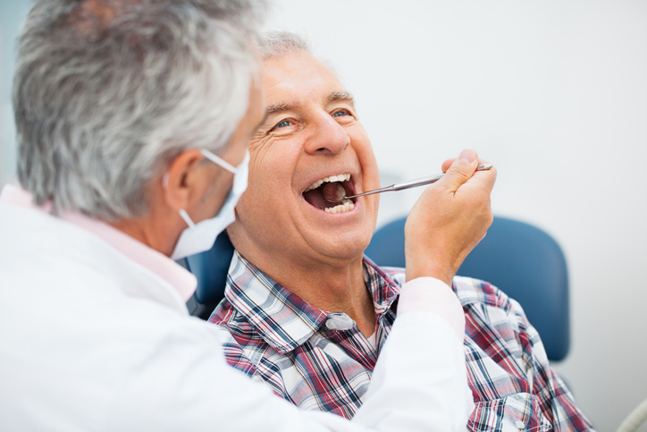 A gray-haired patient opens his mouth wide for the dentist.