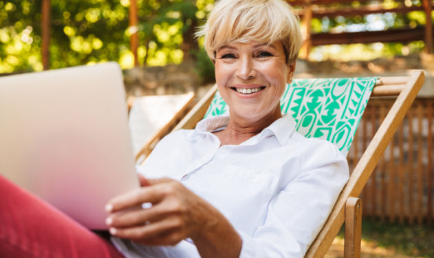A woman sitting outdoors with her laptop and smiling