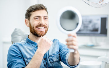 man smiling in mirror at periodontists office