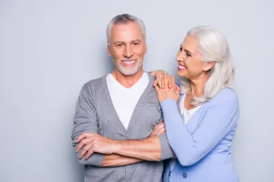 Dental implants: senior couple smiling on gray background.