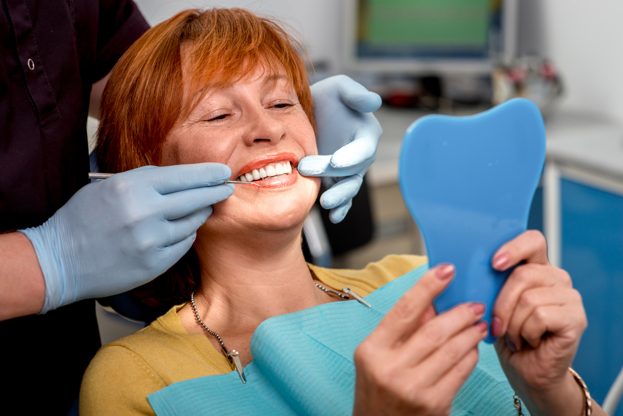 Female denture patient holding a hand mirror, smiling in dental chair