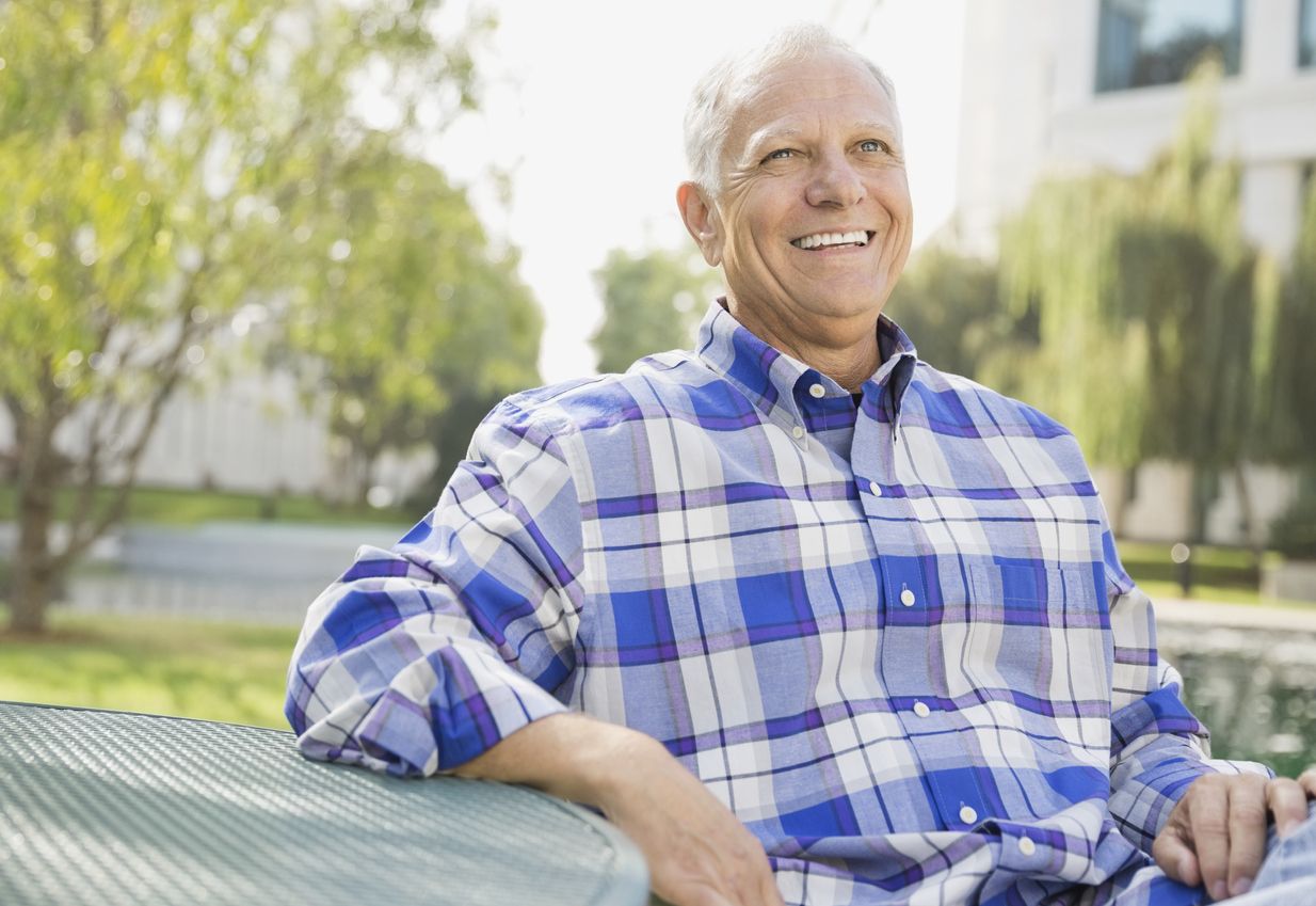 Senior man outside smiling while sitting at a table