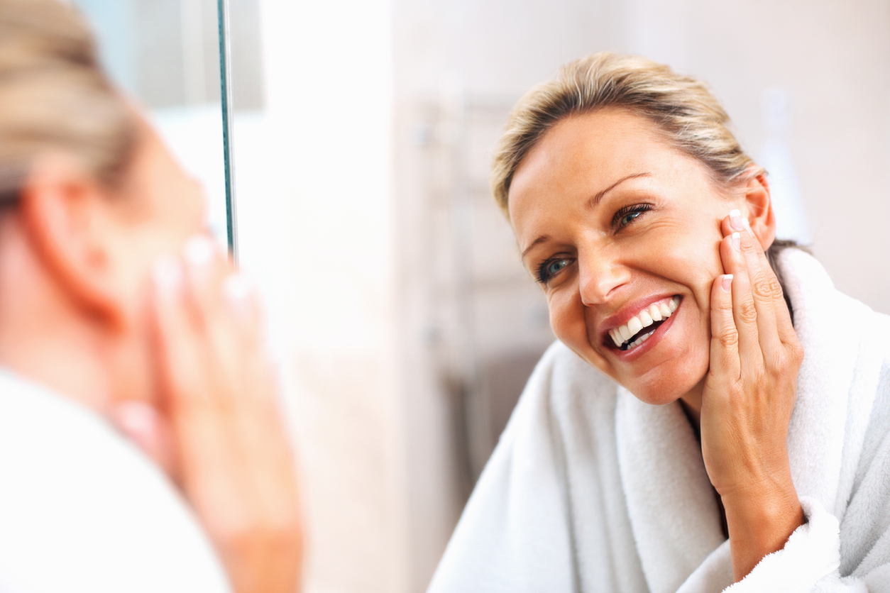 Woman smiling in bathroom mirror touching her face