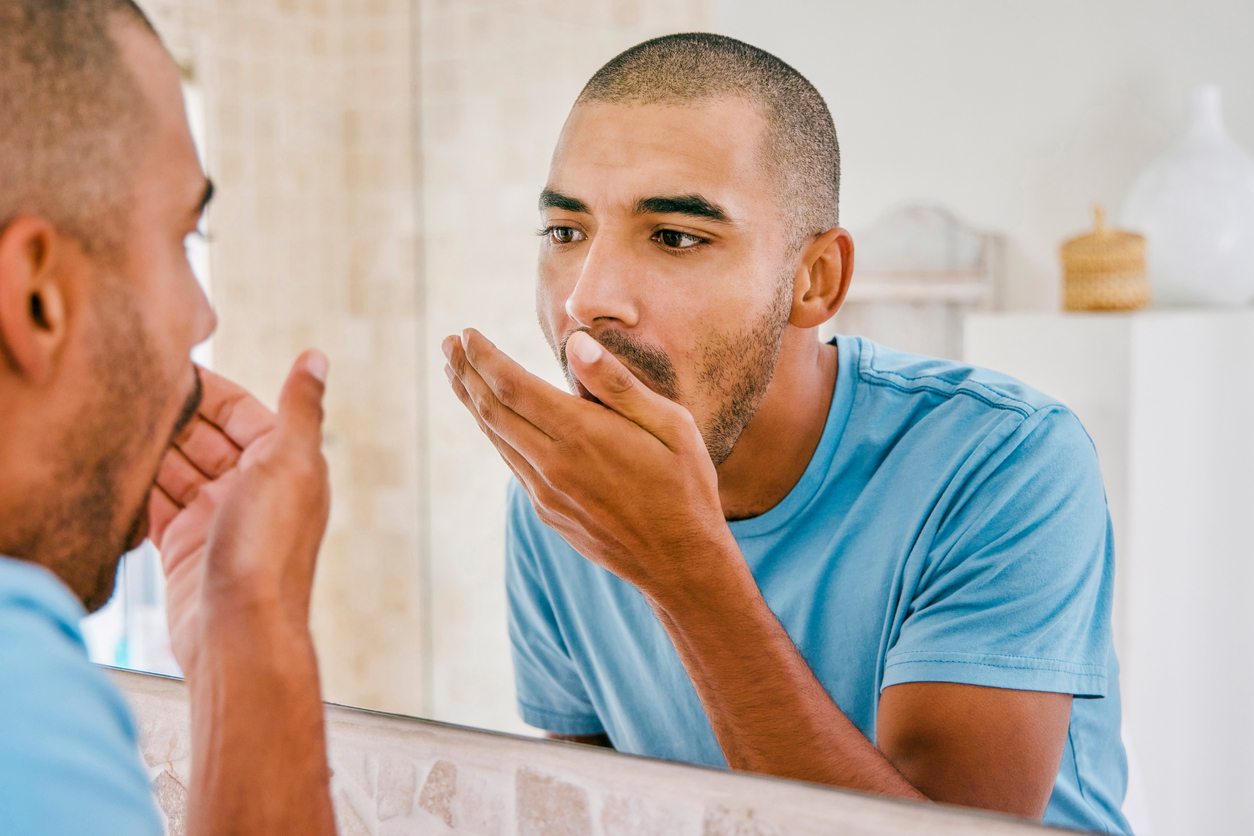 Man checking his breath in the bathroom looking in the mirror