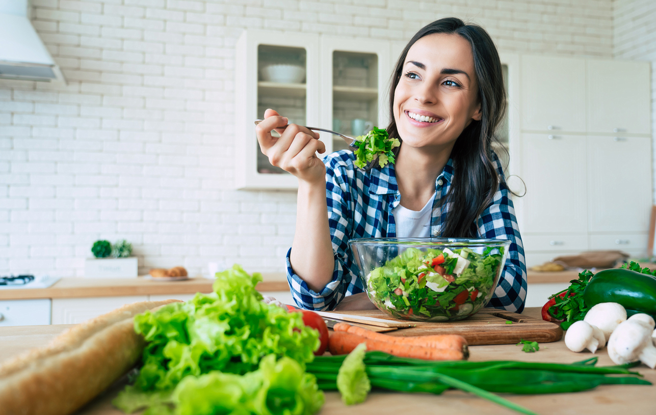 Woman eating a big green salad and holding a green drink