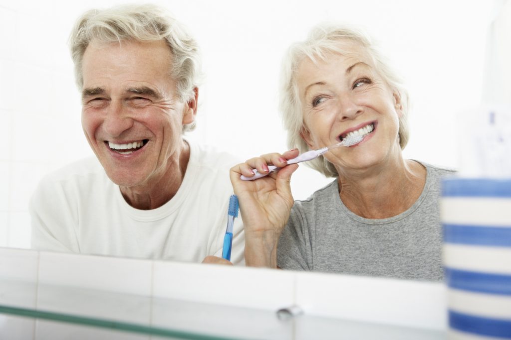 Senior couple In bathroom brushing teeth and smiling