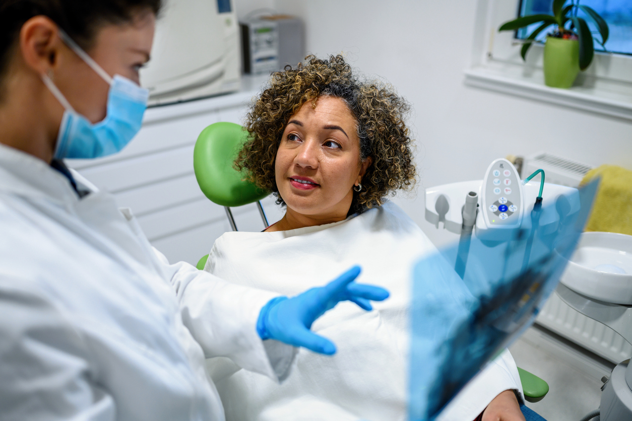 female dental implant patient in dental chair speaking with hygienist