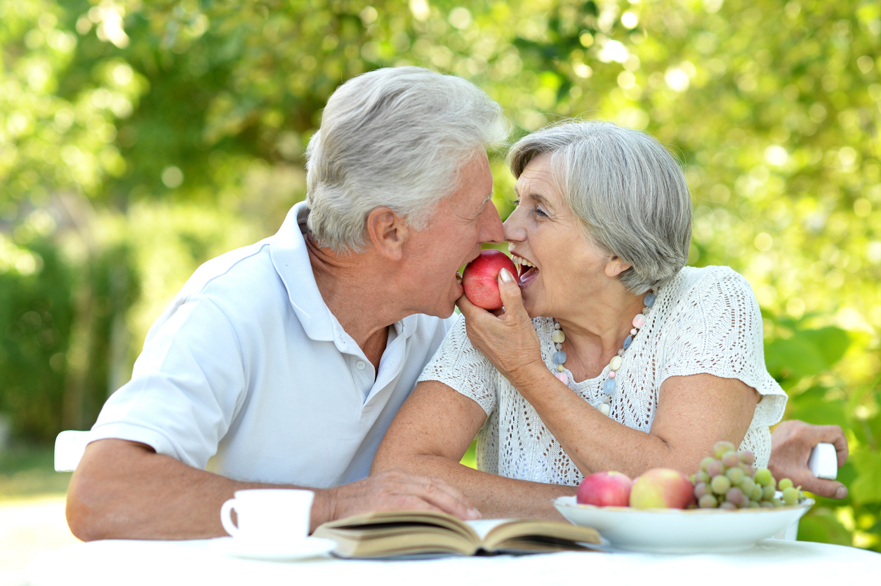 a senior couple eating the same apple at the same time outside