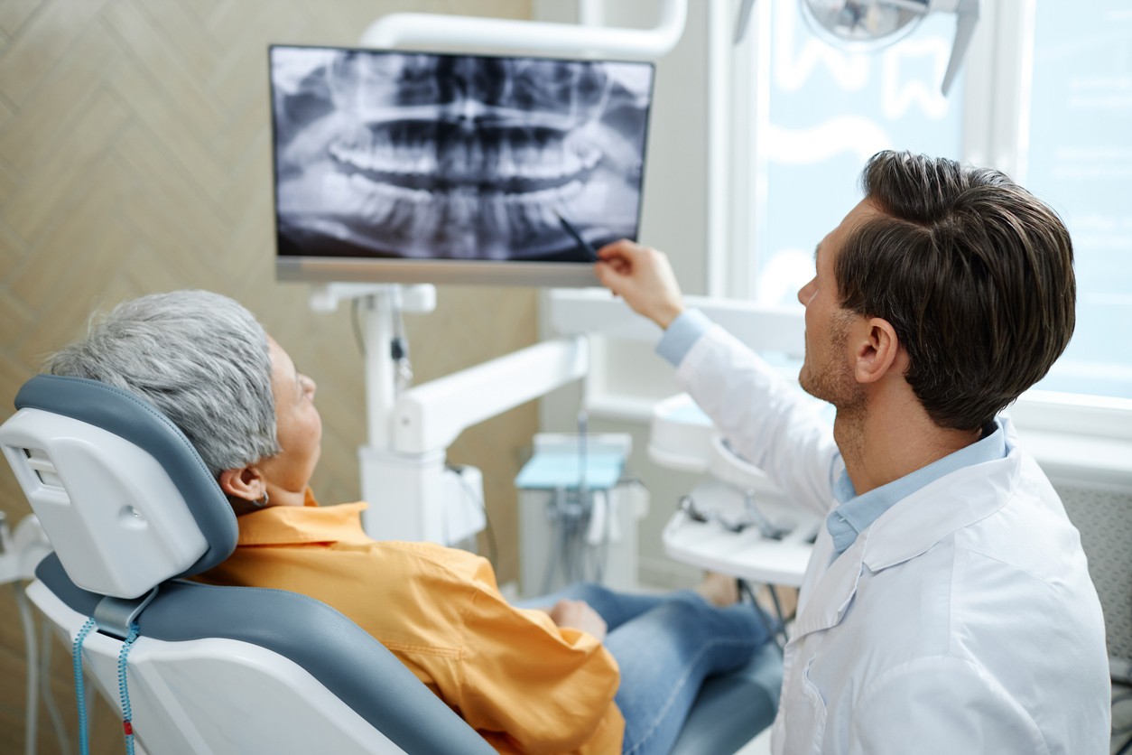 Back view of female periodontal patient and a male dentist pointing at tooth X-ray image on screen